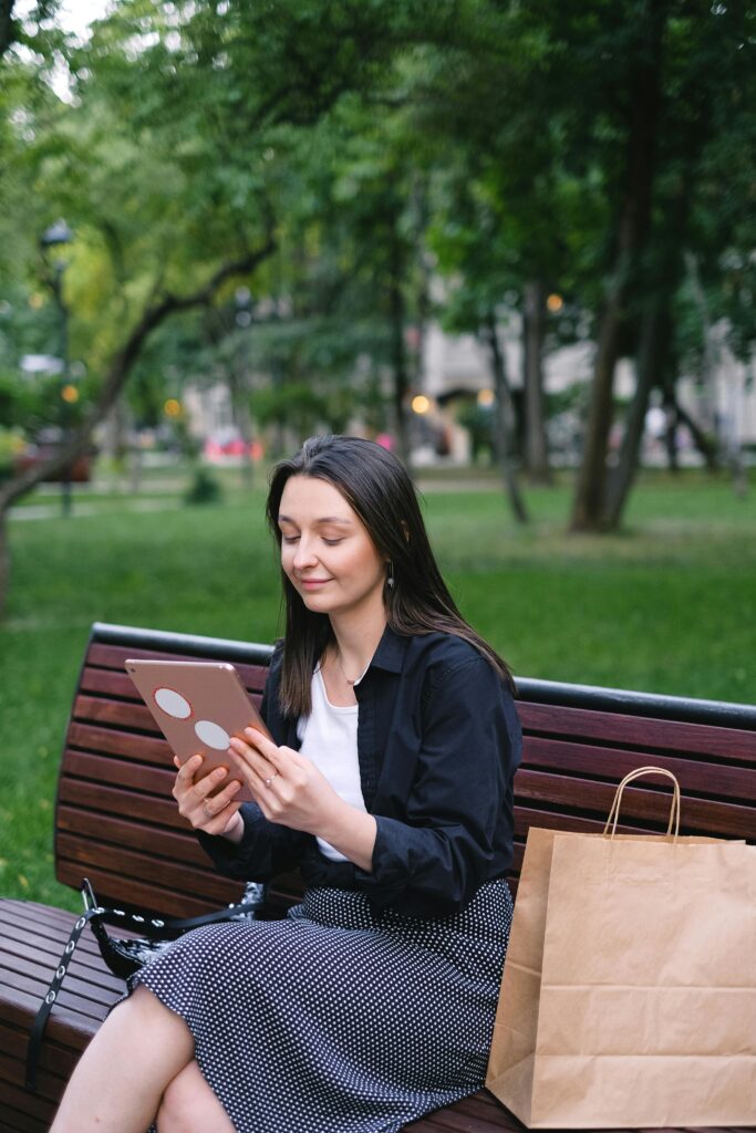 Young woman using a tablet while sitting on a park bench. Relaxed and connected lifestyle.