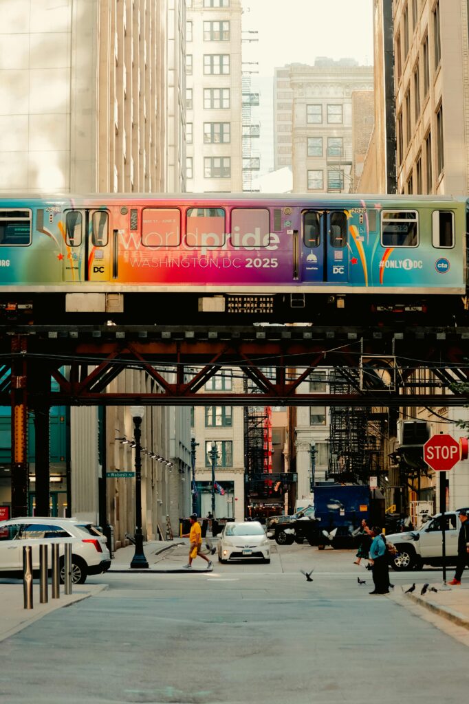 Vibrant city scene with a colorful train on elevated tracks amidst tall buildings.